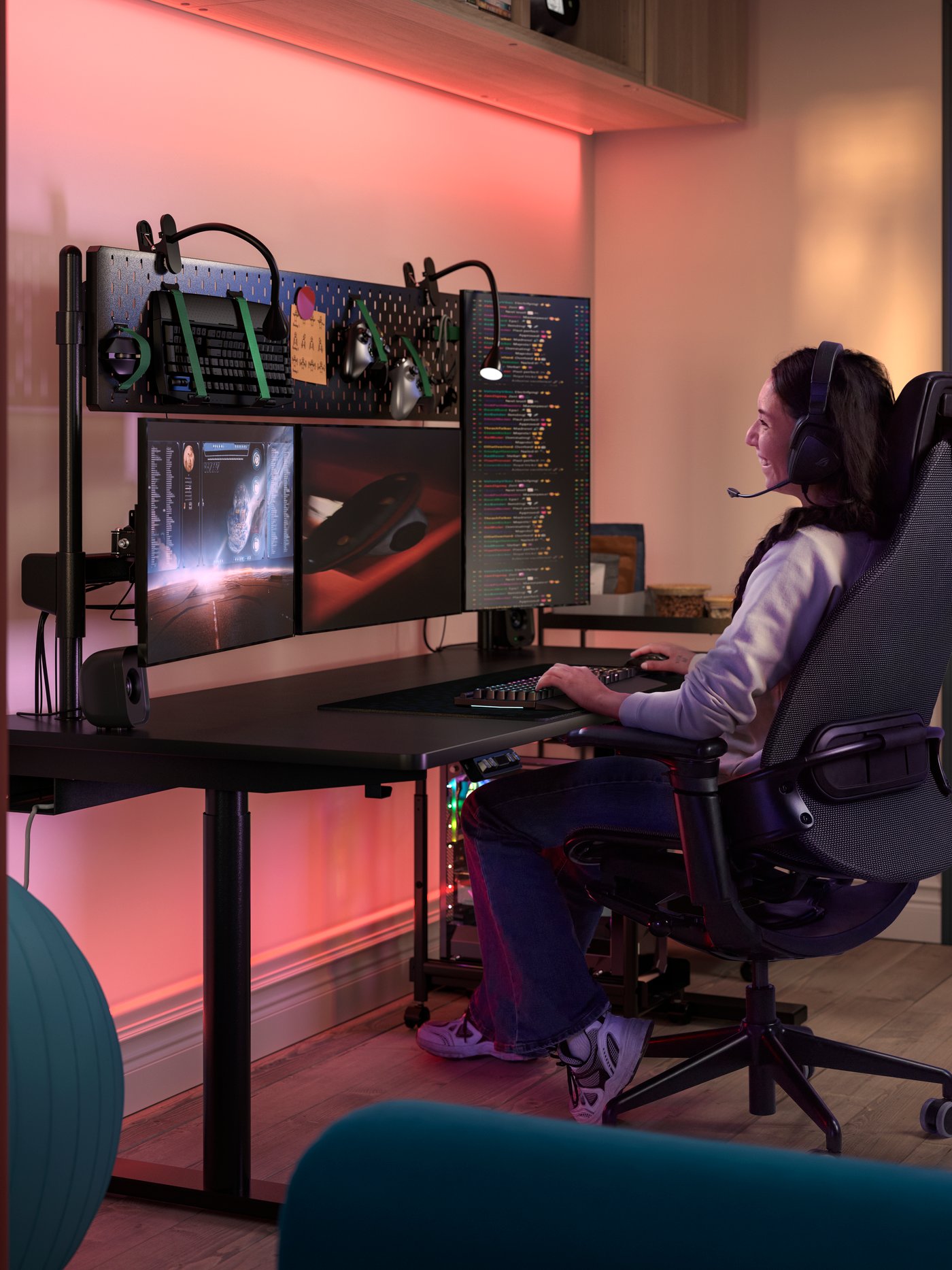 Een persoon zit in een BÄSTBOLL gamingstoel aan een MÅLOMRÅDE gamingbureau. Aan het bureau zijn NÄVLINGE klemlampen bevestigd.