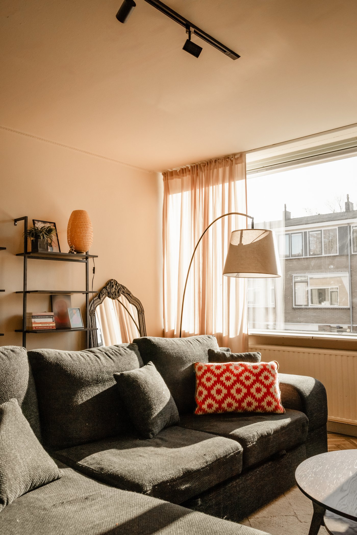 Woonkamer met donkere hoekbank, daarnaast een vloerlamp met boog en een ronde salontafel.