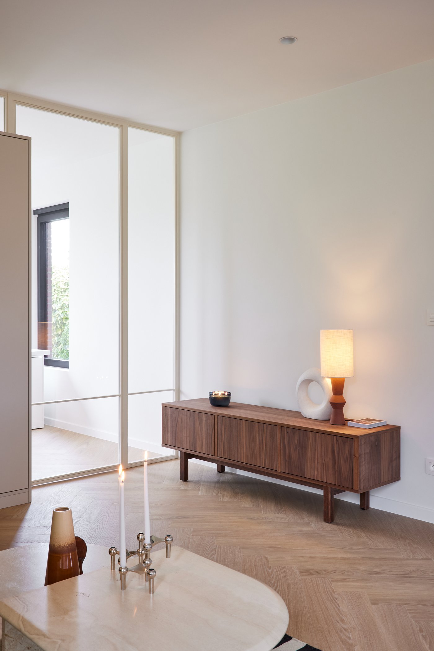 Stijlvolle woonkamer met visgraatvloer, marmeren tafel en houten dressoir.