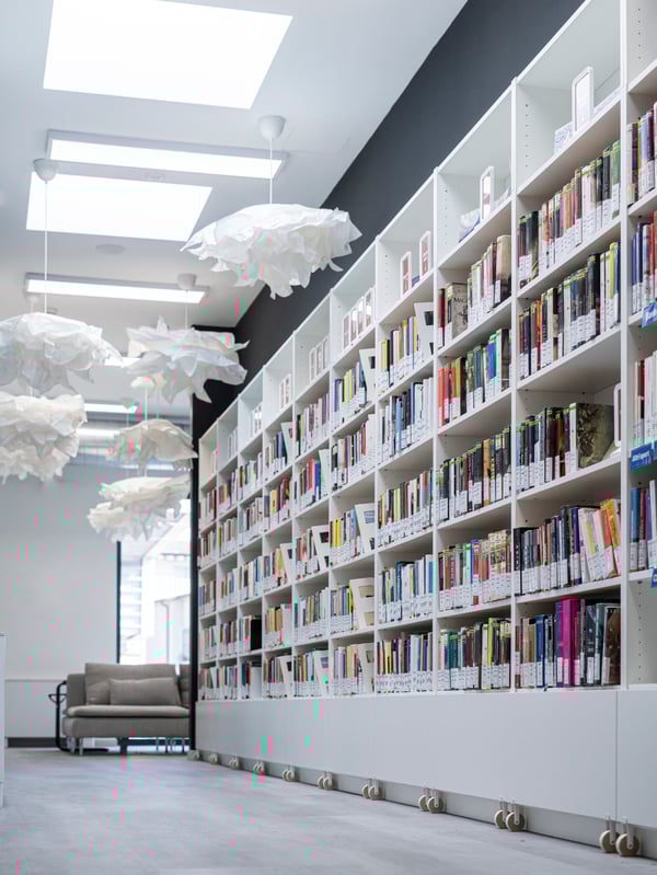Una libreria con cassetto BILLY di colore bianco collocata in una delle sale della Biblioteca comunale di Brescia Roncadelle. La stanza è illuminata da sei lampade a sospensione con paralumi KRUSNING e sullo sfondo si intravedono ampie vetrate e un elemento a 3 posti SÖDERHAMN.