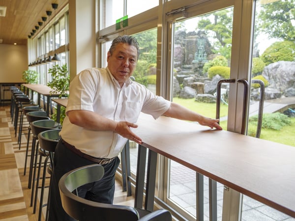 大きな窓際のカウンターで立つ人物。外には庭が広がり、自然を感じられる開放的な空間