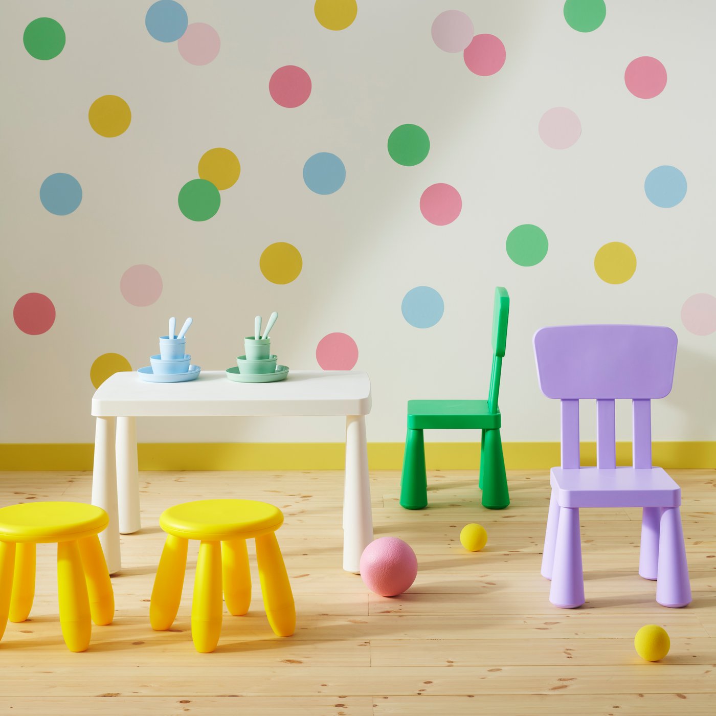 A white table surrounded by two yellow stools and chairs in bright green and lilac from the MAMMUT series, by a spotted wall.