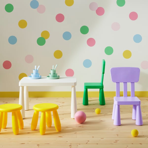 A white table surrounded by two yellow stools and chairs in bright green and lilac from the MAMMUT series, by a spotted wall.