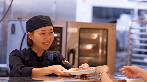 厨房でスタッフが料理を盛り付けた皿をお客さまに手渡している様子。