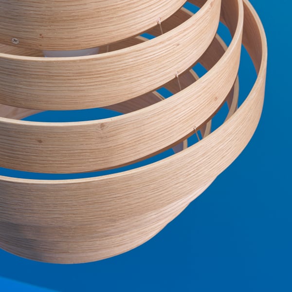 A close-up of the seven veneer rings that make up the DYKARKLOCKA pendant lampshade with a bright blue background.