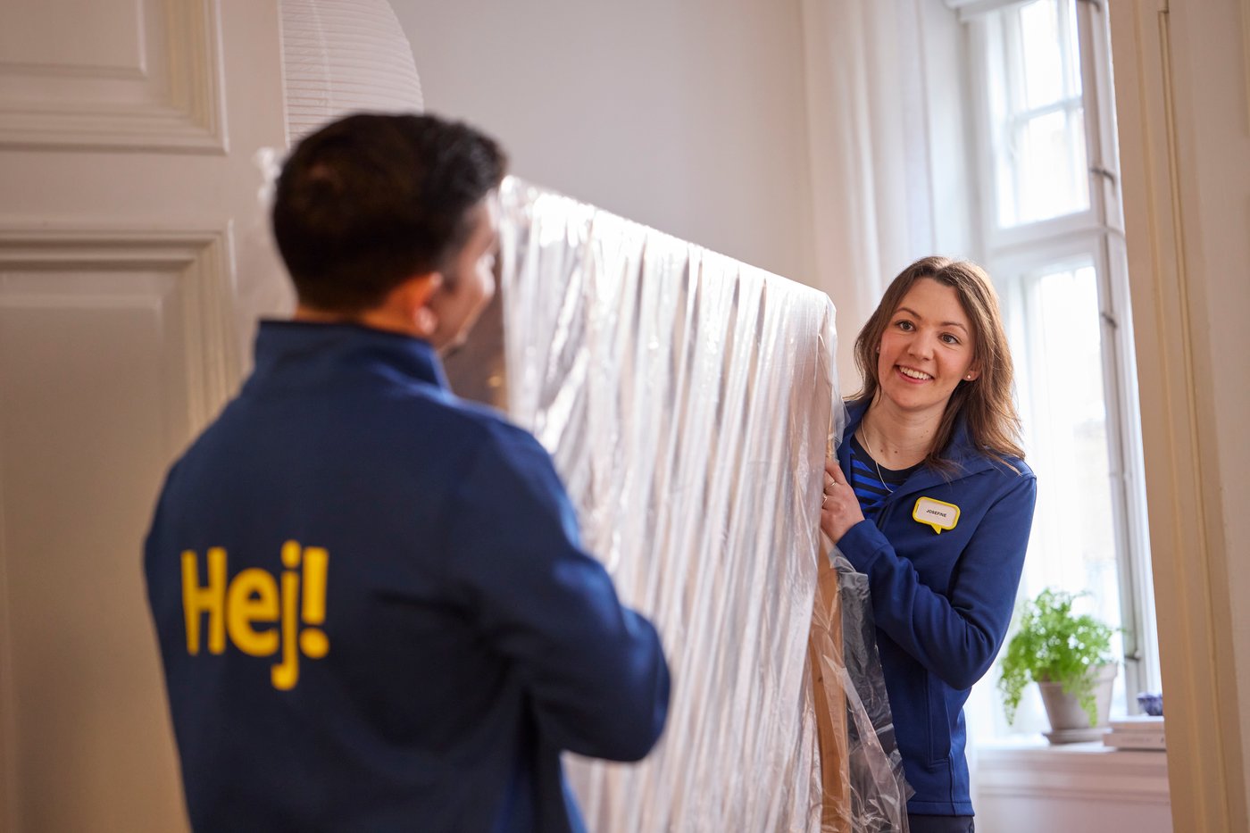 Zwei IKEA Mitarbeiter:innen tragen ein Bettgestell.