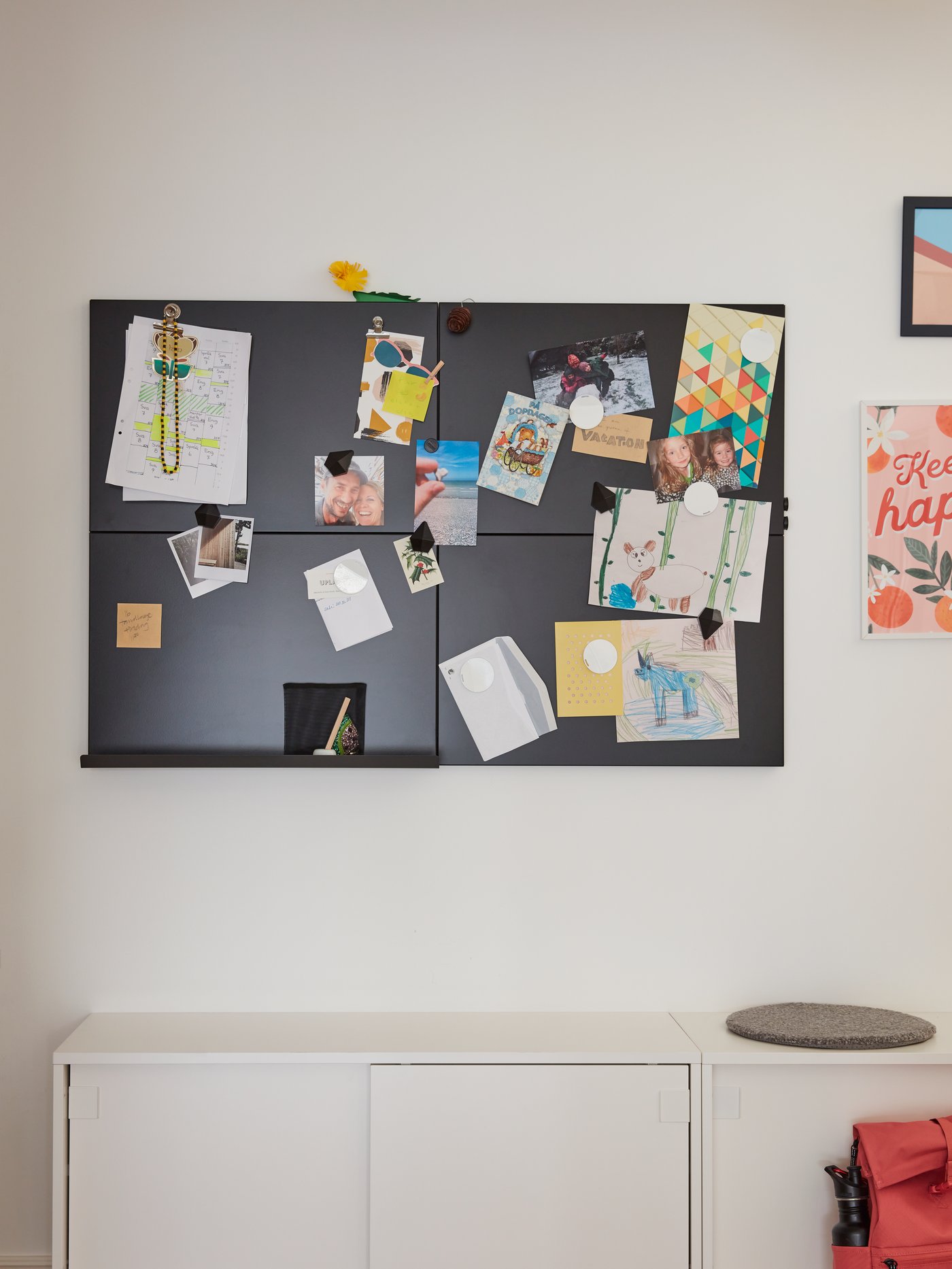Vista frontal de un conjunto de 4 pizarras de notas SVENSÅS negras con fotos y postales adheridas a su superficie por imanes. Las pizarras están colgadas en un muro blanco, sobre un mueble bajo MACKAPÄR. 