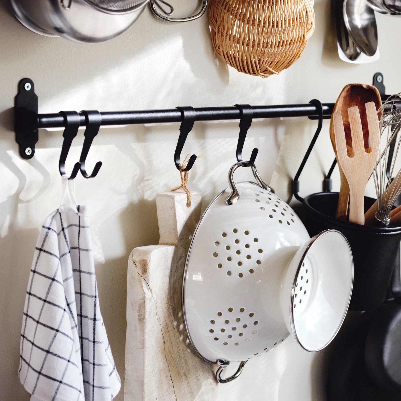 Från en svart HULTARP hänger en kökshandduk, en skärbräda, ett vitt durkslag och köksredskap i en svart HULTARP.