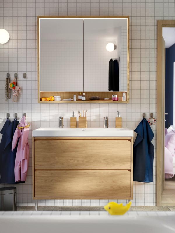En spegel från LINDBYN hänger mellan två vägglampor från FRIHULT ovanför ett vitt tvättställ från RÄTTVIKEN med två lådor.