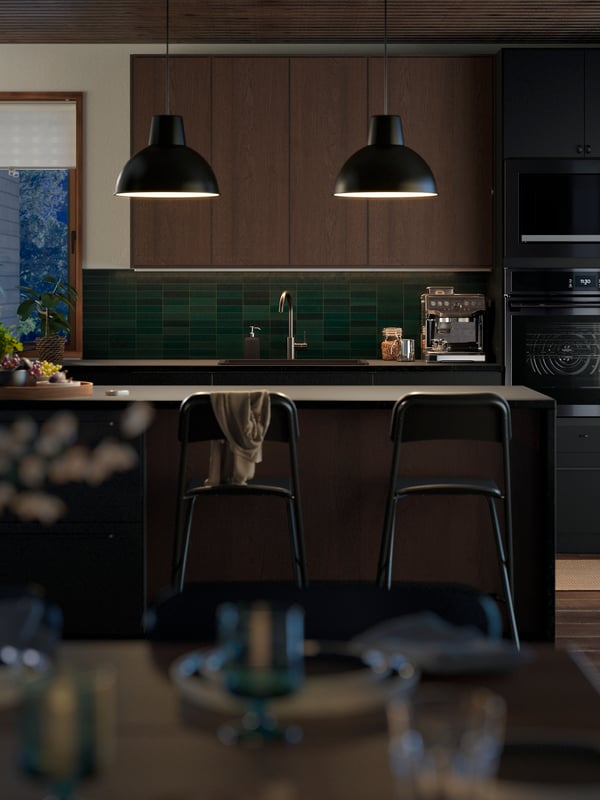 A modern kitchen with green tiles and SINARP kitchen fronts in brown. Two pendant lamps are lighting up a kitchen island.
