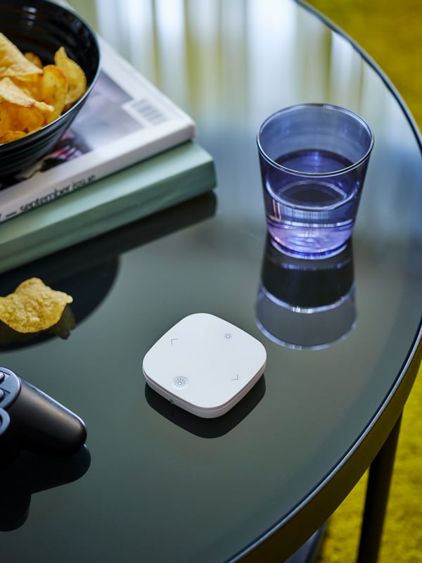 The IKEA Home smart remote control STYRBAR is laying on a FRÖTORP glass table.