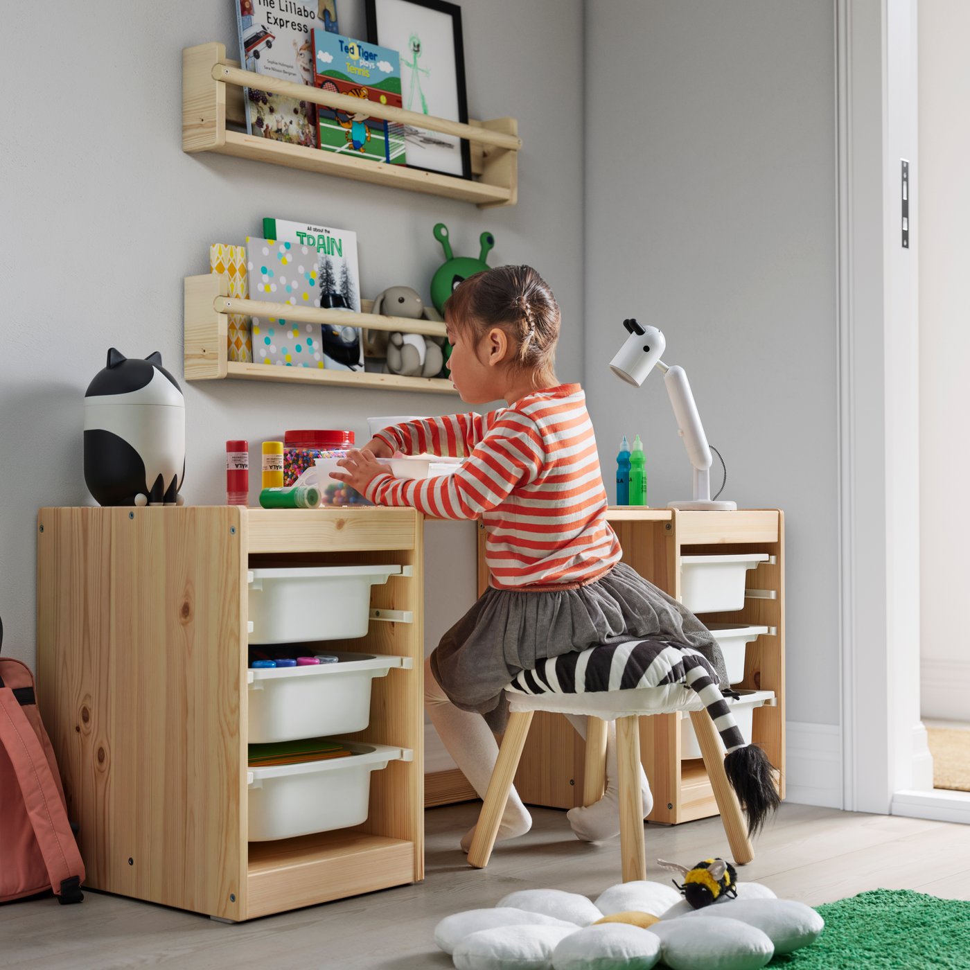 child sitting on a stool while playing with toys on top of her desk. The desk has lots of storage space