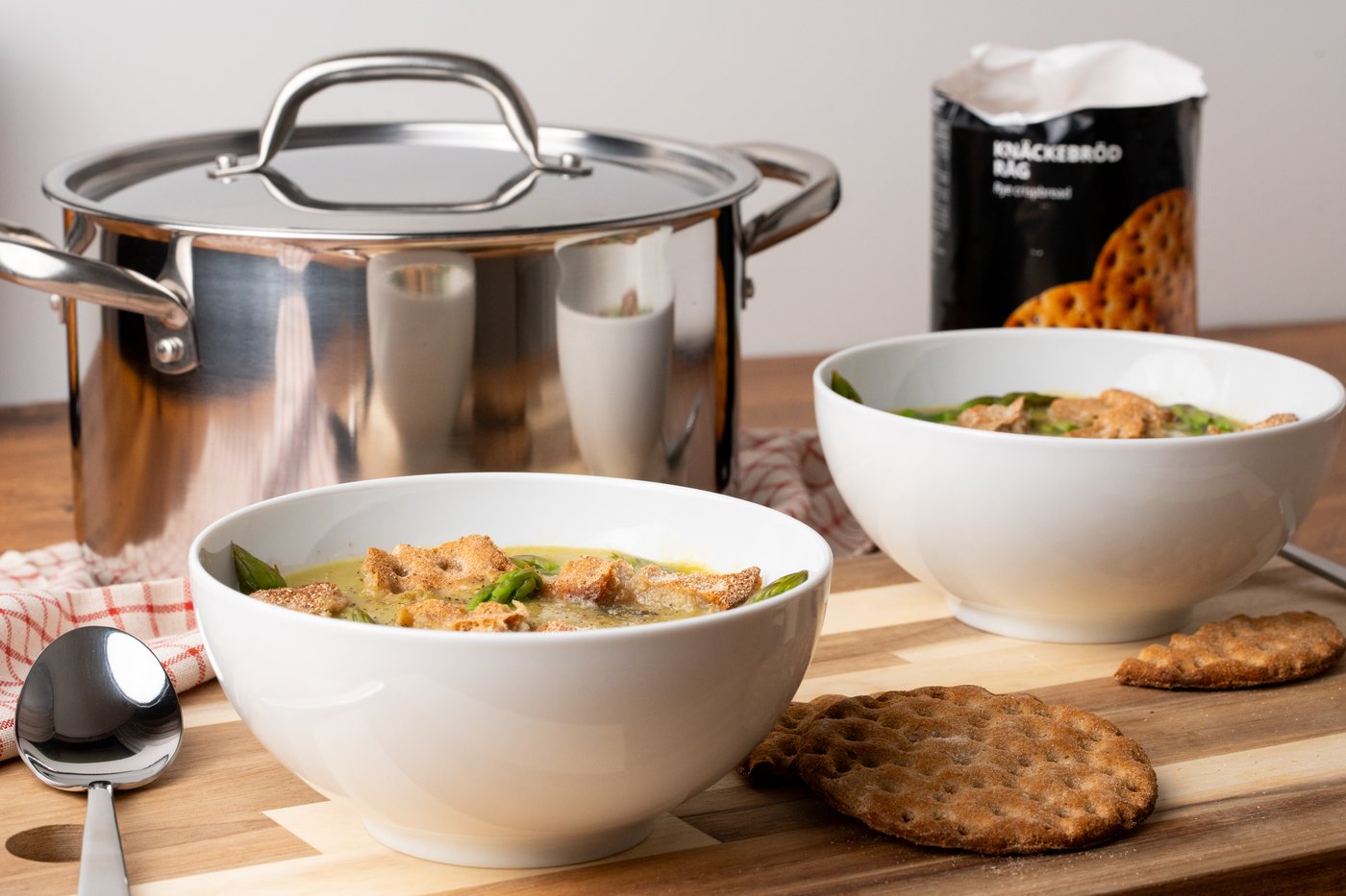 Eine Spargelsuppe mit Knäckebrot-Crunch auf einem Holztisch präsentiert.