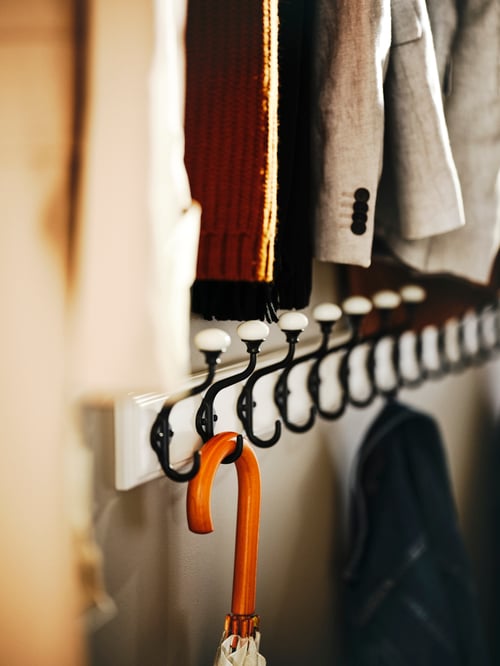 Close-up of multiple, white racks with hooks. An umbrella hangs on a hook in the foreground. Above the racks are clothes.
