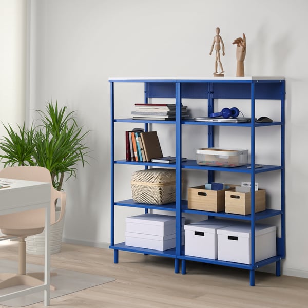 Modrá sestava regálů s bílou deskou na vrchu, zaplněná boxy a dekoracemi.