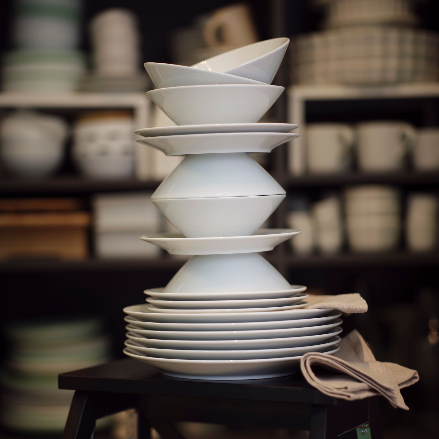 All pieces of a white IKEA 365+ 18-piece service are playfully stacked on top of each other on a black stepladder.