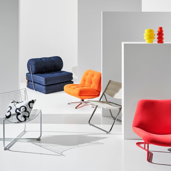 Five different chairs from the Nytillverkad collection are placed in a white room. Among them a blue VÅRKUMLA chair bed.