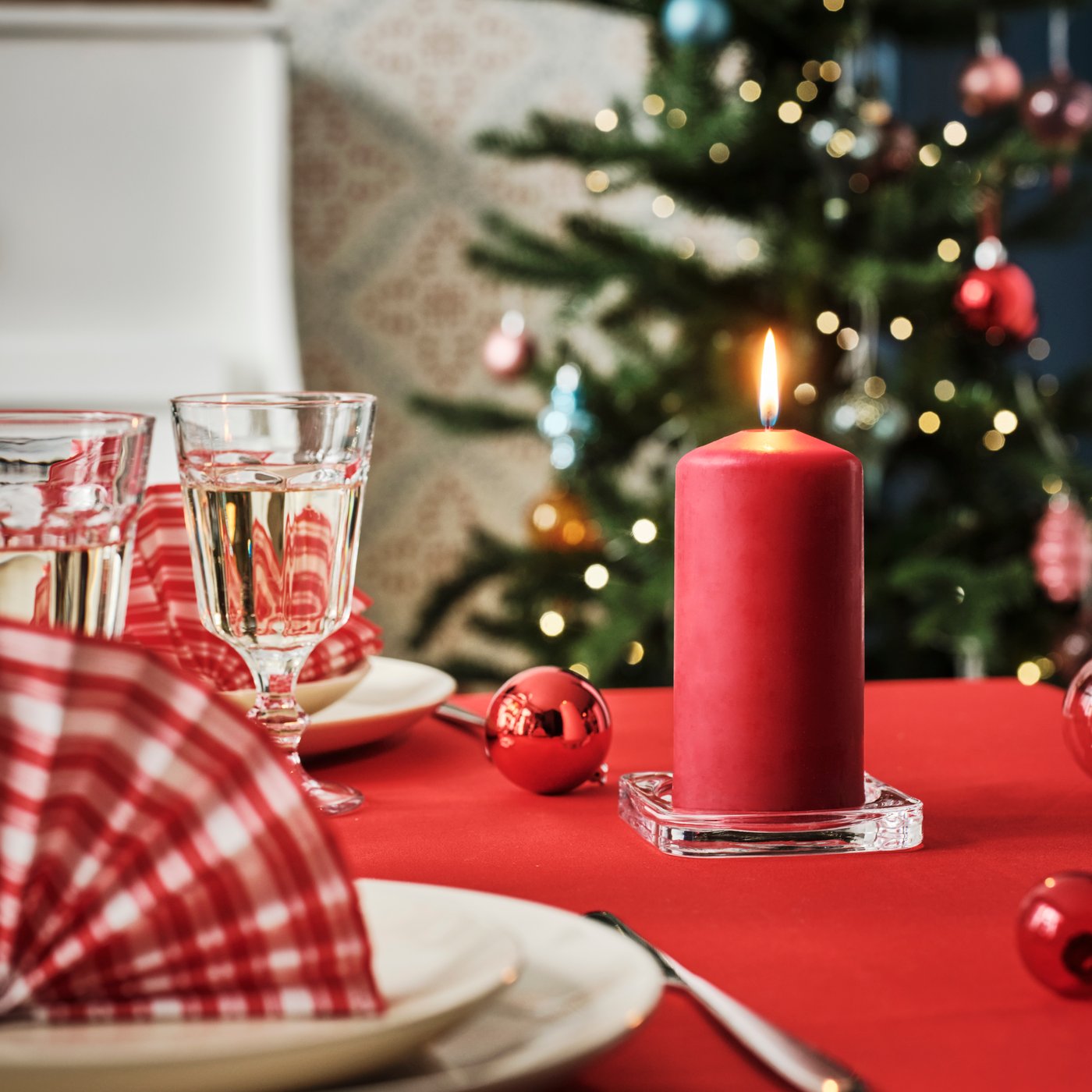 Ett rött FENOMEN blockljus på ett juldukat bord med röd duk.