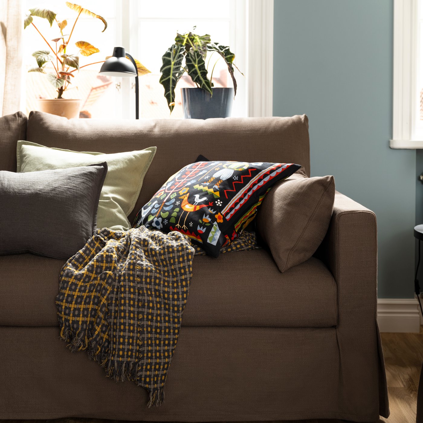 Un jeté FLIKBRUNÖRT et quelques coussins, dont un avec une housse de coussin TRATTKAKTUS multicolore, sont posés sur une HYLTARP canapé.