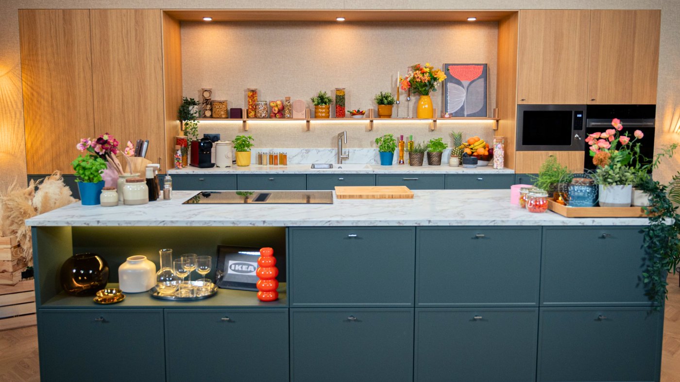 Une cuisine moderne aux tons bois et bleu foncé, décorée de plantes et d’objets colorés, avec un grand îlot en marbre au centre