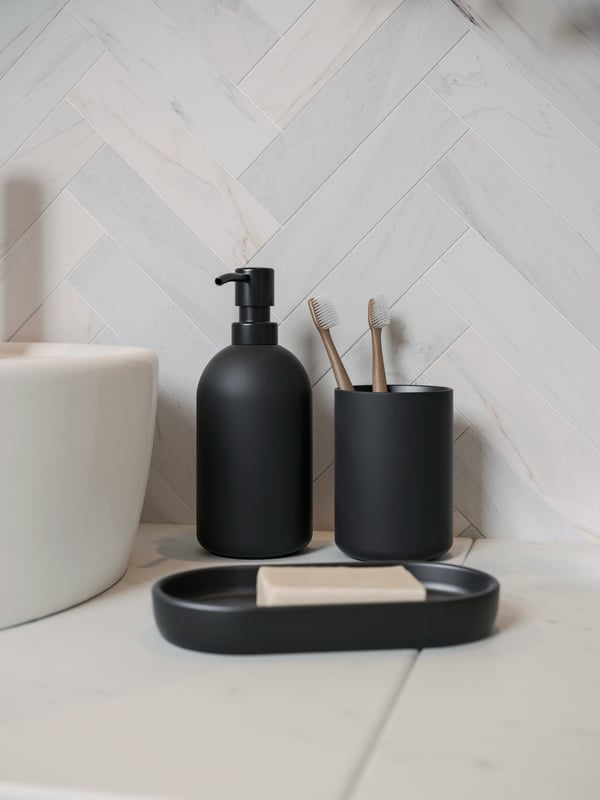 Un set da bagno GANSJÖN di colore con nero da 3 pezzi nel bagno. Accanto, si intravede un lavabo bianco.