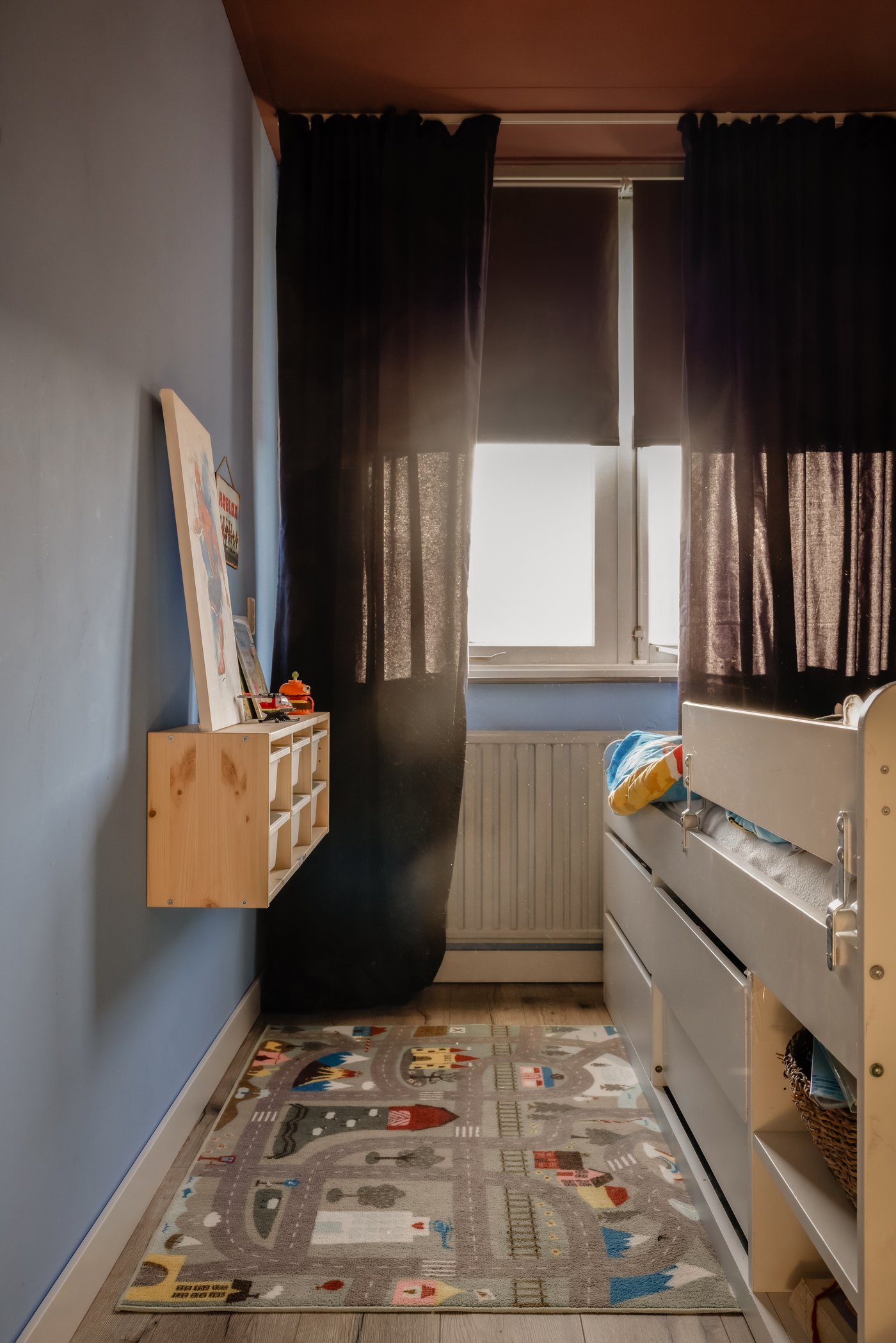 Kinderkamer met SLÄKT/NATTAPA kinderbed. Aan de muur hangt een TROFAST opbergsysteem. Op de grond ligt een VALLABY vloerkleed met daarop wegen.
