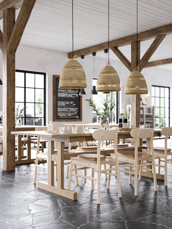 Wooden chairs and a long wooden dining table with three pendant lamp shades made of seagrass above it.