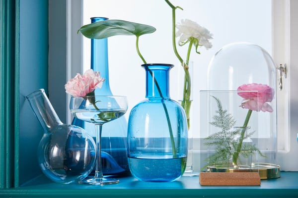 Several different shaped blue and clear glass vases and an IKEA BEGÅVNING glass dome on a window sill.