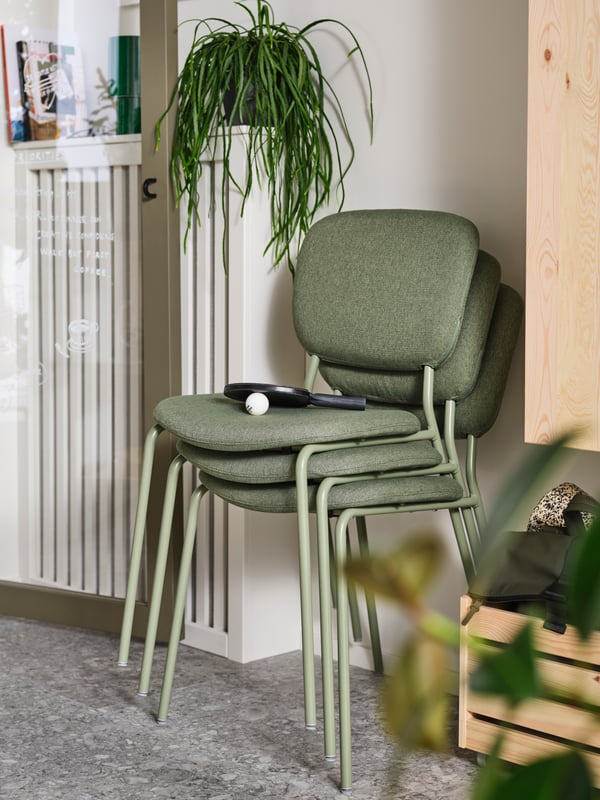 Three VIHALS chairs are stacked together beside an IVAR storage box on wheels and an IVAR cabinet on the wall.