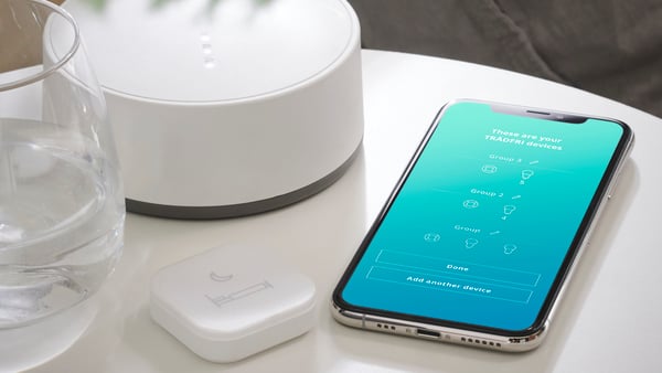 A TRÅDFRI remote control next to a smart phone with the Home Smart app