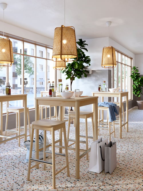 Kitchen area featuring multiple, square bar tables, beige bar stools, beige pendant lamps, and bowls.