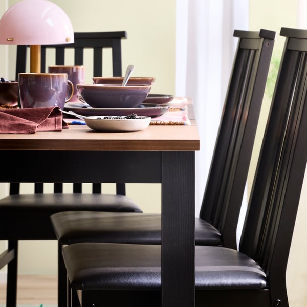 Une table extensible ÅLHULT en noir/brun, entourée de chaises assorties, est accompagnée de tasses et d'assiettes colorées GLADELIG.