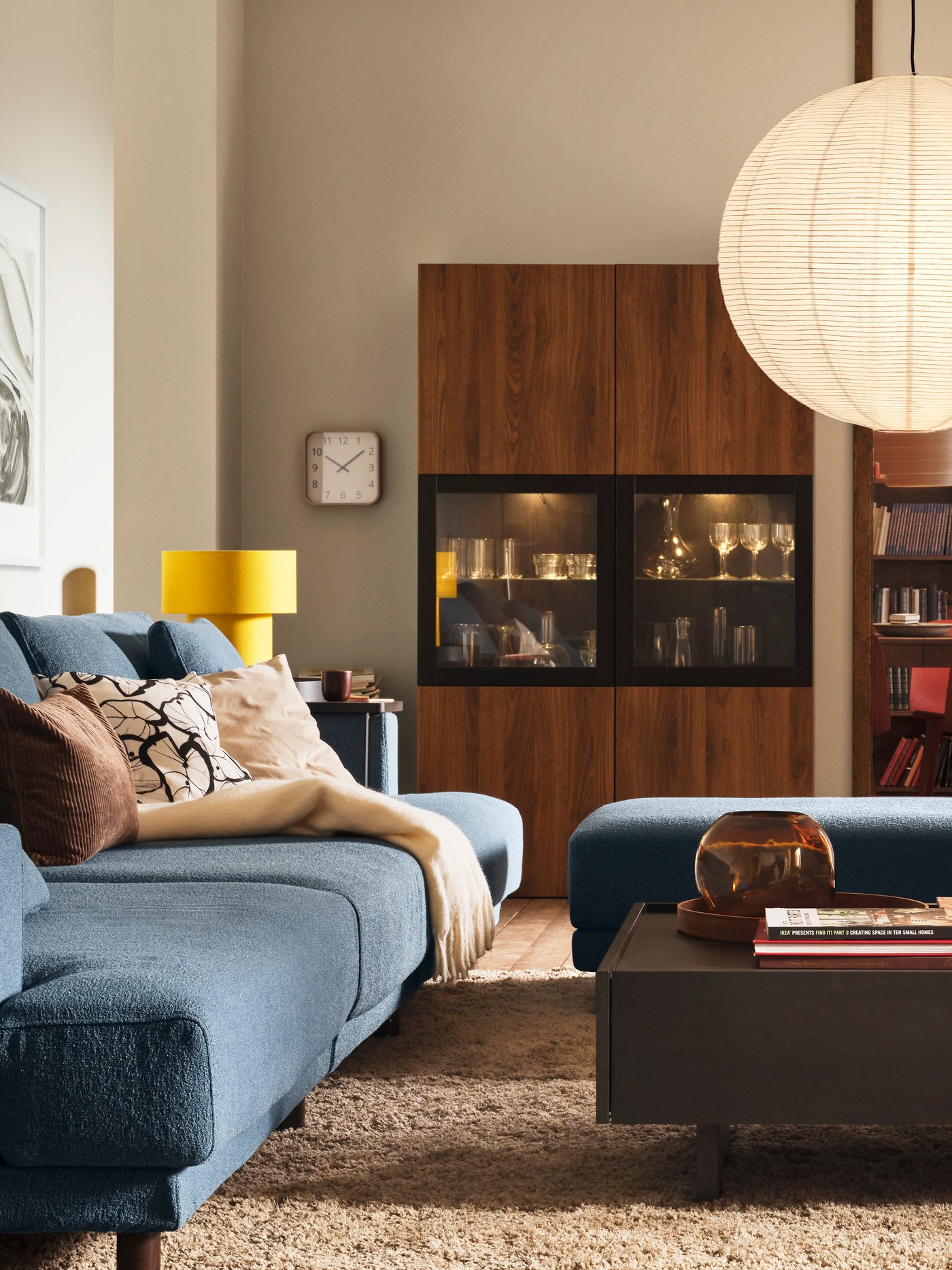 Stolik kawowy TRANERED ustawiony przed czteroosobową sofą modułową UPPÅKRA obok kombinacji do przechowywania BESTÅ z przeszklonymi drzwiami.