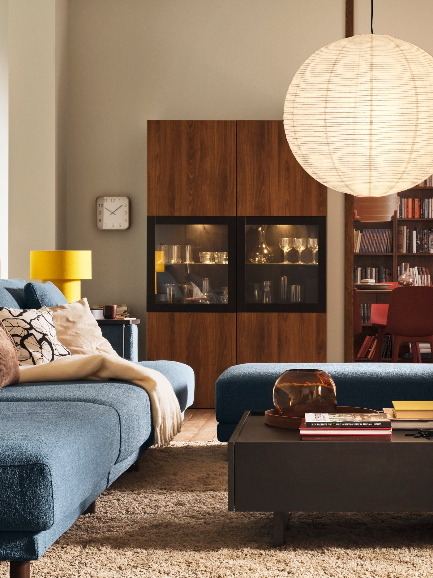 Ett TRANERED soffbord står framför en UPPÅKRA modulsoffa med 4,5 sittplatser, nära en BESTÅ förvaringskombination med glasdörrar