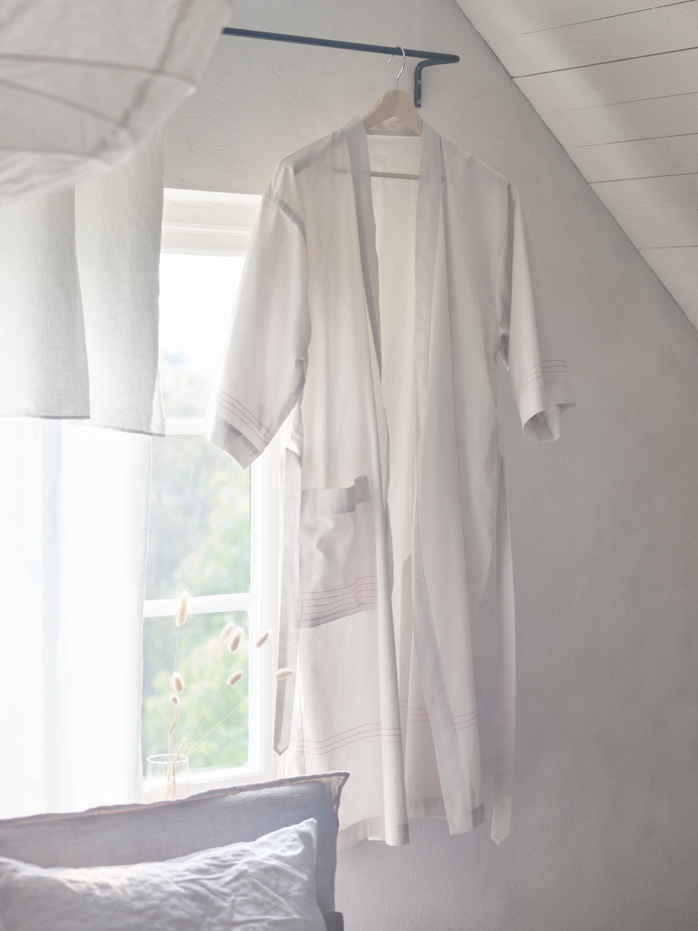 A VÅRDANDE 100% cotton kimono hangs from a curtain pole in a bedroom with white walls.
