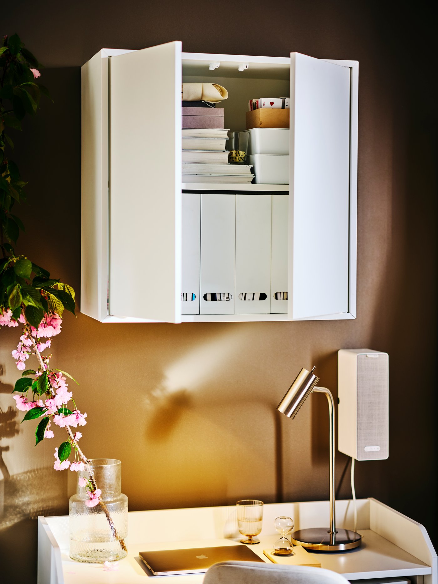 Mueble EKET blanco con dos puertas parcialmente abiertas con libros en su interior, encima de un escritorio HAUGA blanco con una lámpara de trabajo VIRRMA
