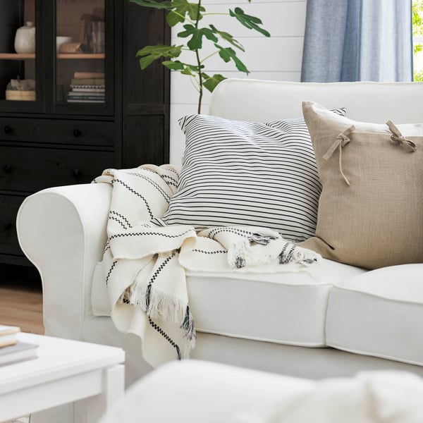 A zoomed in part of a white EKTORP sofa with pillows and a blanket