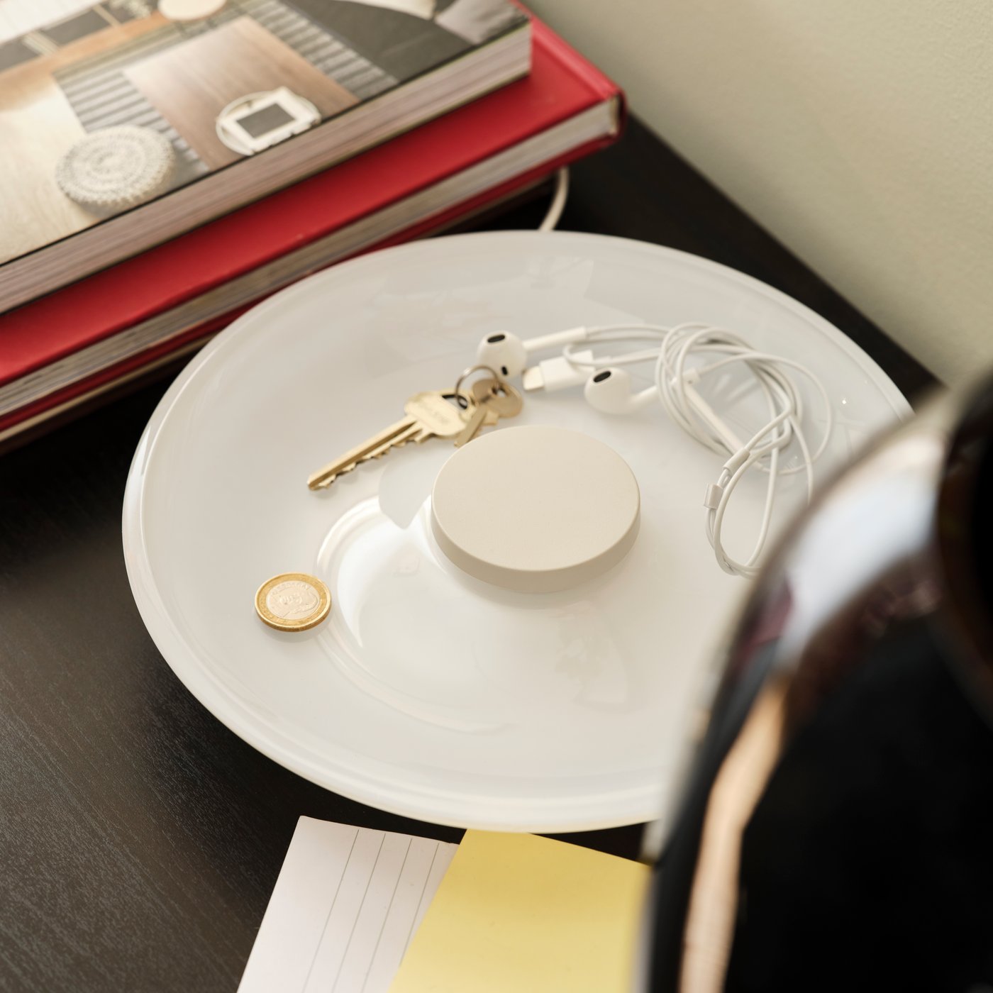 Keys and other small objects lie on the bowl of a VÄSTMÄRKE wireless charger with lighting which is not lit up.