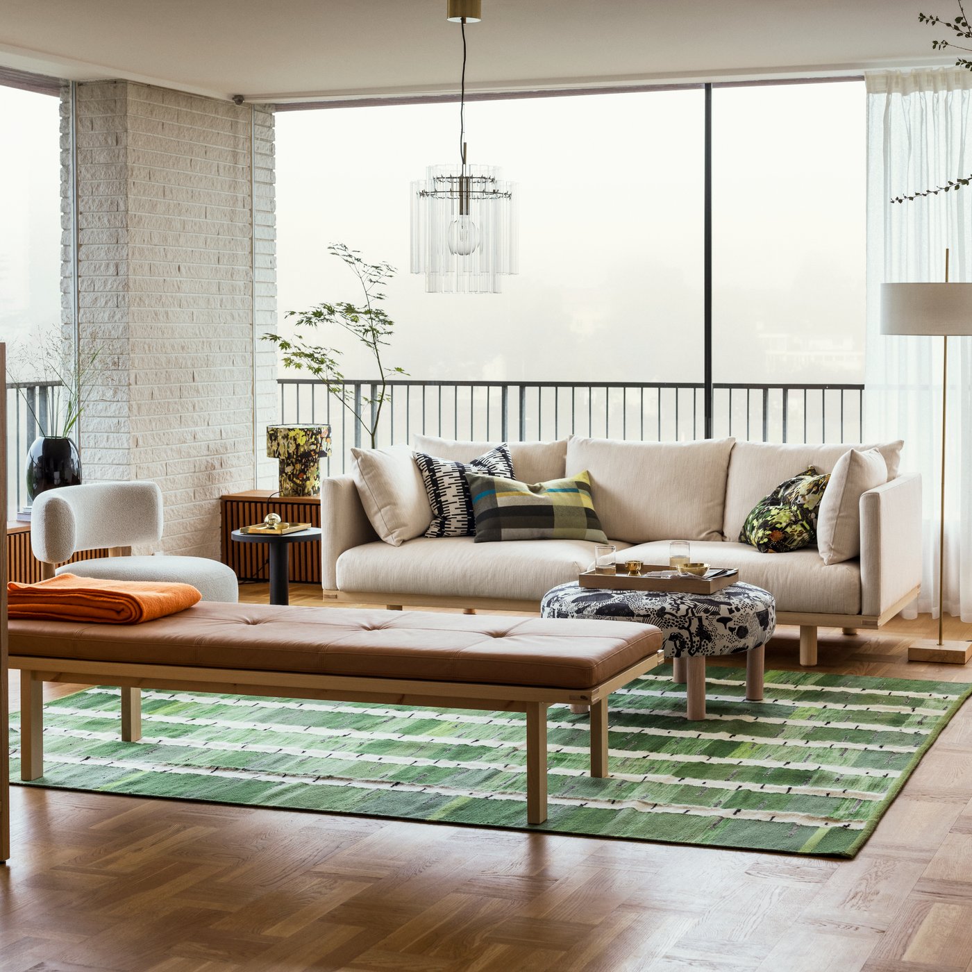 A bright living room with a beige STOCKHOLM 2025 3-seat sofa by a bench and pouffe sitting on a green, black, and white rug.