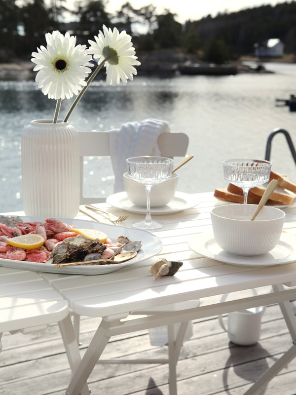 Et hvidt opdækket robust havebord på en sommerhus terrasse med havet i baggrunden.