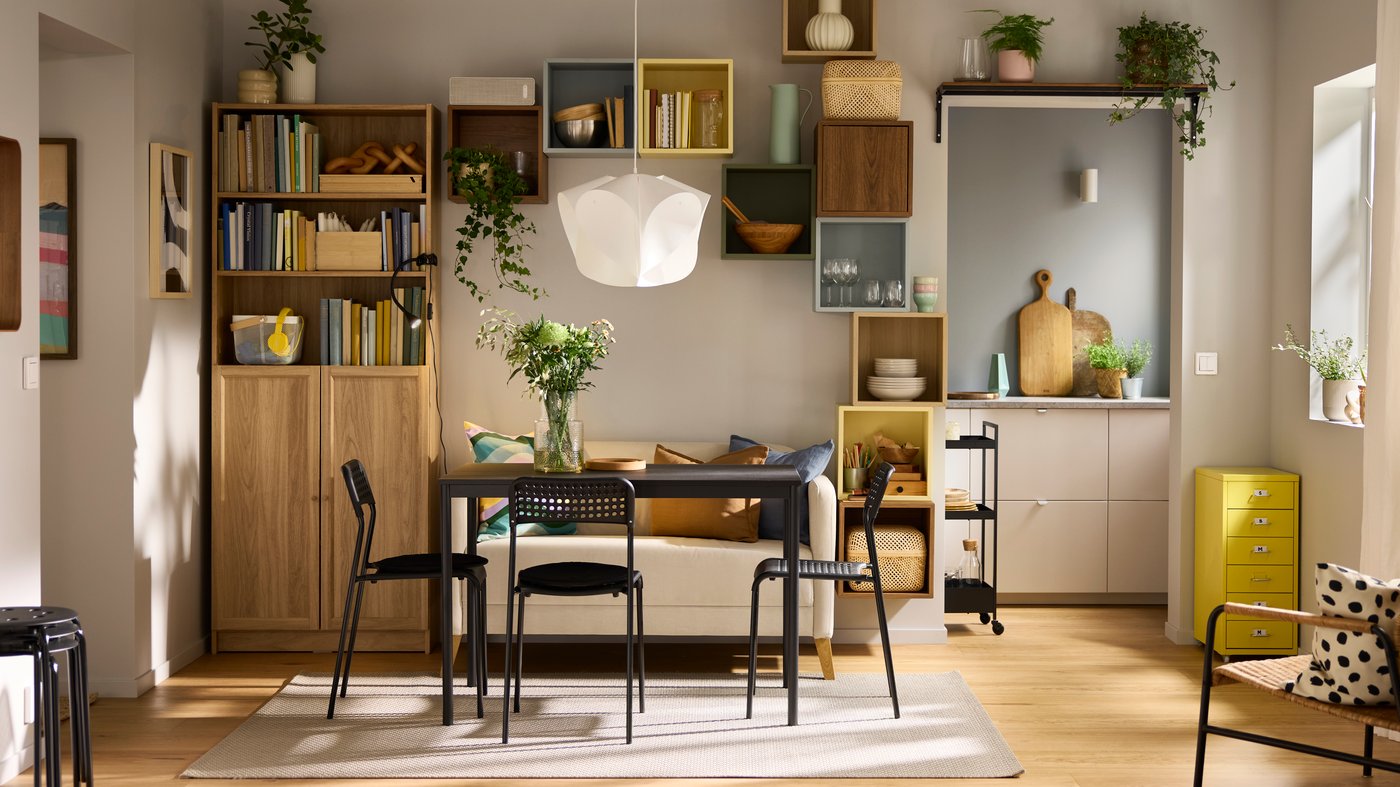 A black SANDSBERG table, three chairs and a sofa are placed in a living room with a BILLY bookcase in the background.