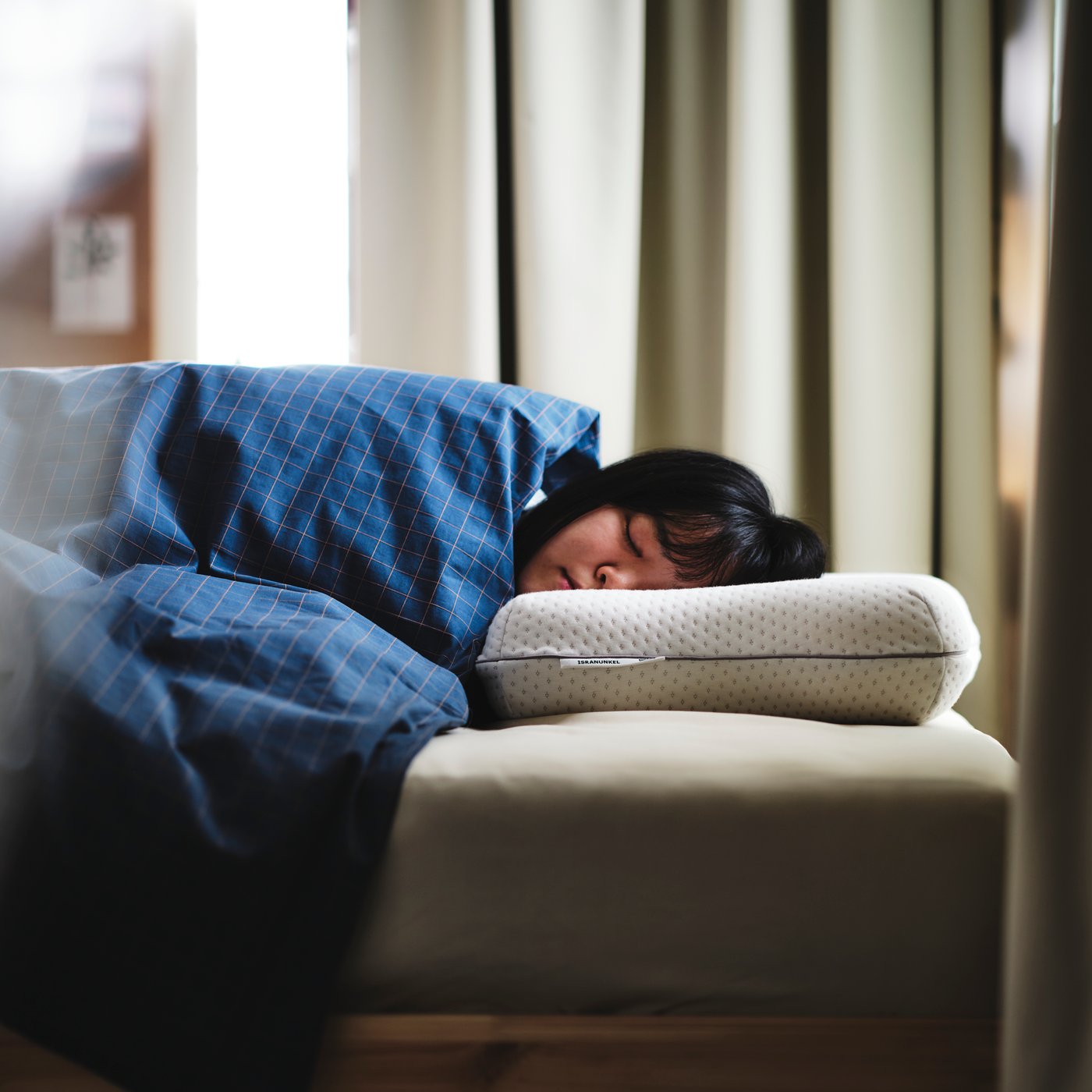 A person asleep under blue/brown DOFTAKLEJA bed linen with their head on an ISRANUNKEL multi-position ergonomic pillow.