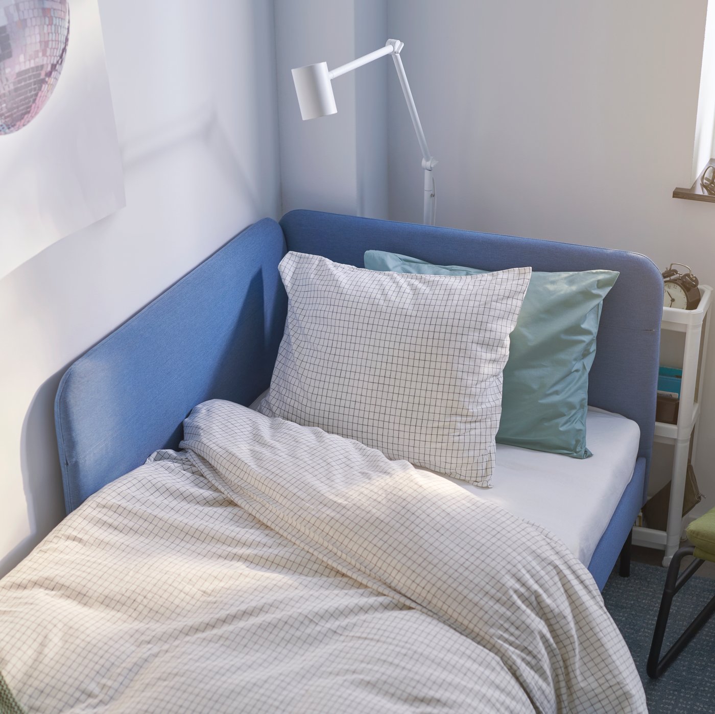 Blaues Bett mit grünem Kissen und weißer Decke.