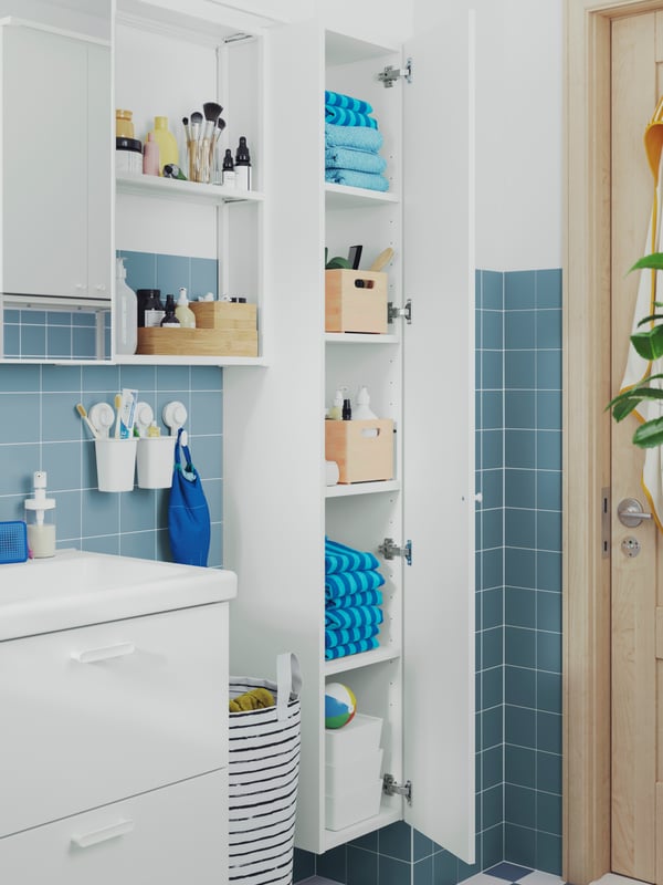 A bathroom with a white ENHET high cabinet with an open door and there are shelves with towels and bathroom products inside.