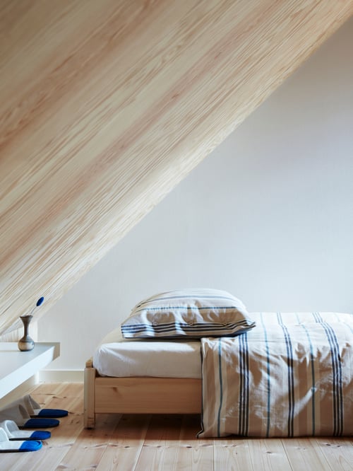 Pine UTÅKER bed frame with mattress and striped bed linens in beige, blue and black, and a dark blue blanket.