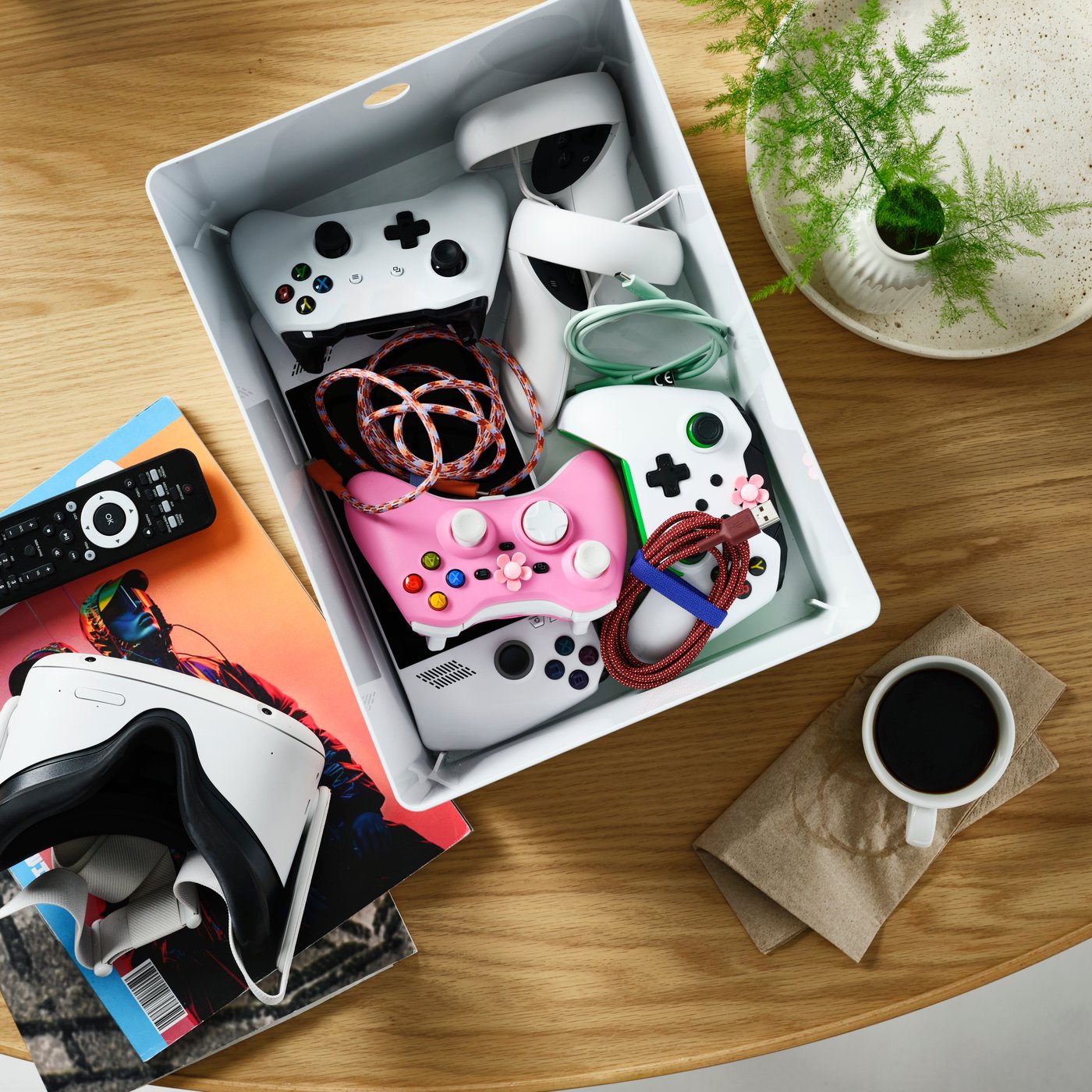 A white KUGGIS box sits on a wooden table. Inside, game controllers, cables and video game accessories are neatly stored.