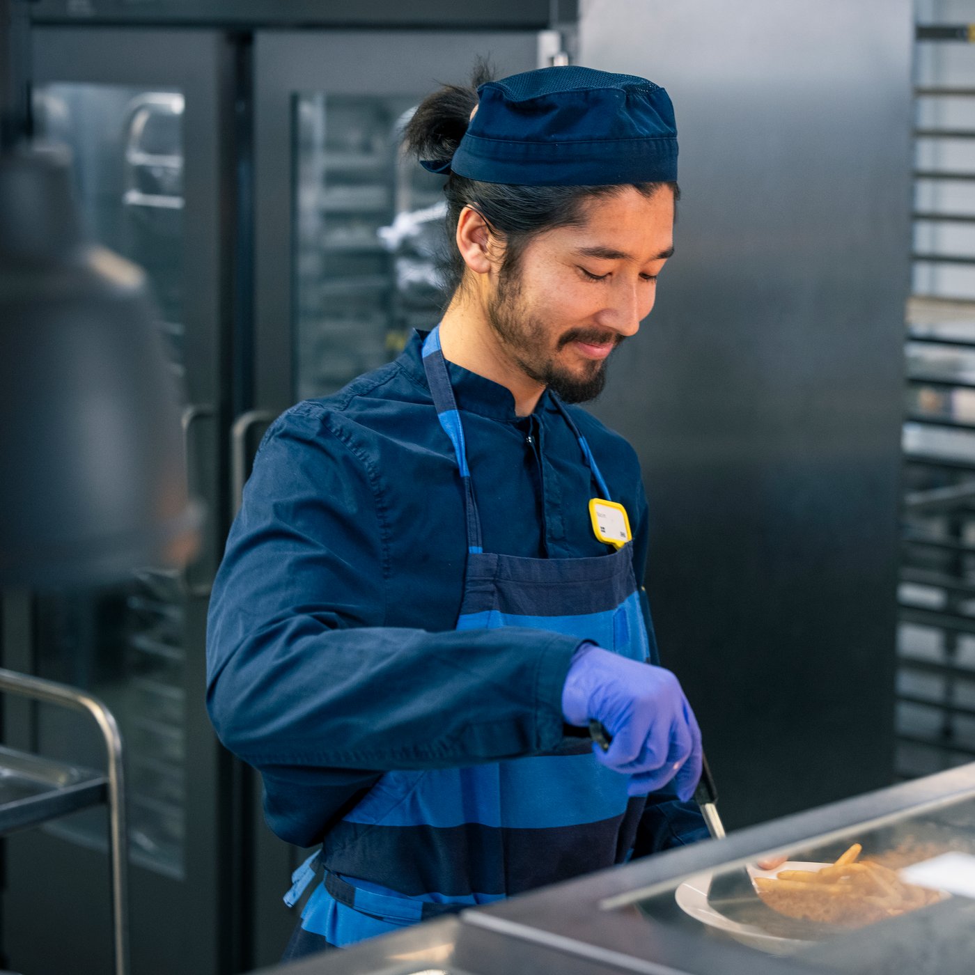 Un collaborateur IKEA souriant portant une tenue de travail bleue et un badge avec son nom.