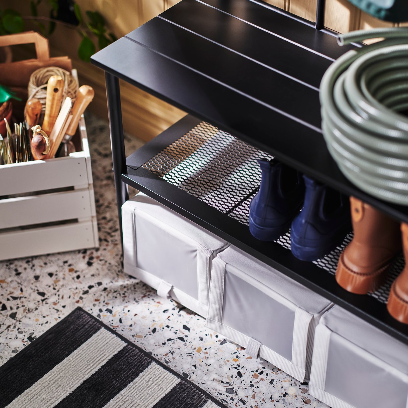 The bottom of a black NIPÅSEN coat rack and bench with shoe storage with three HEMMAFIXARE shoe boxes underneath.