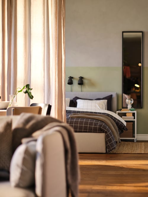 Un appartement à aire ouverte avec une structure de lit rembourrée GLADSTAD contre le mur du fond et une table à abattants KALLHÄLL à droite.