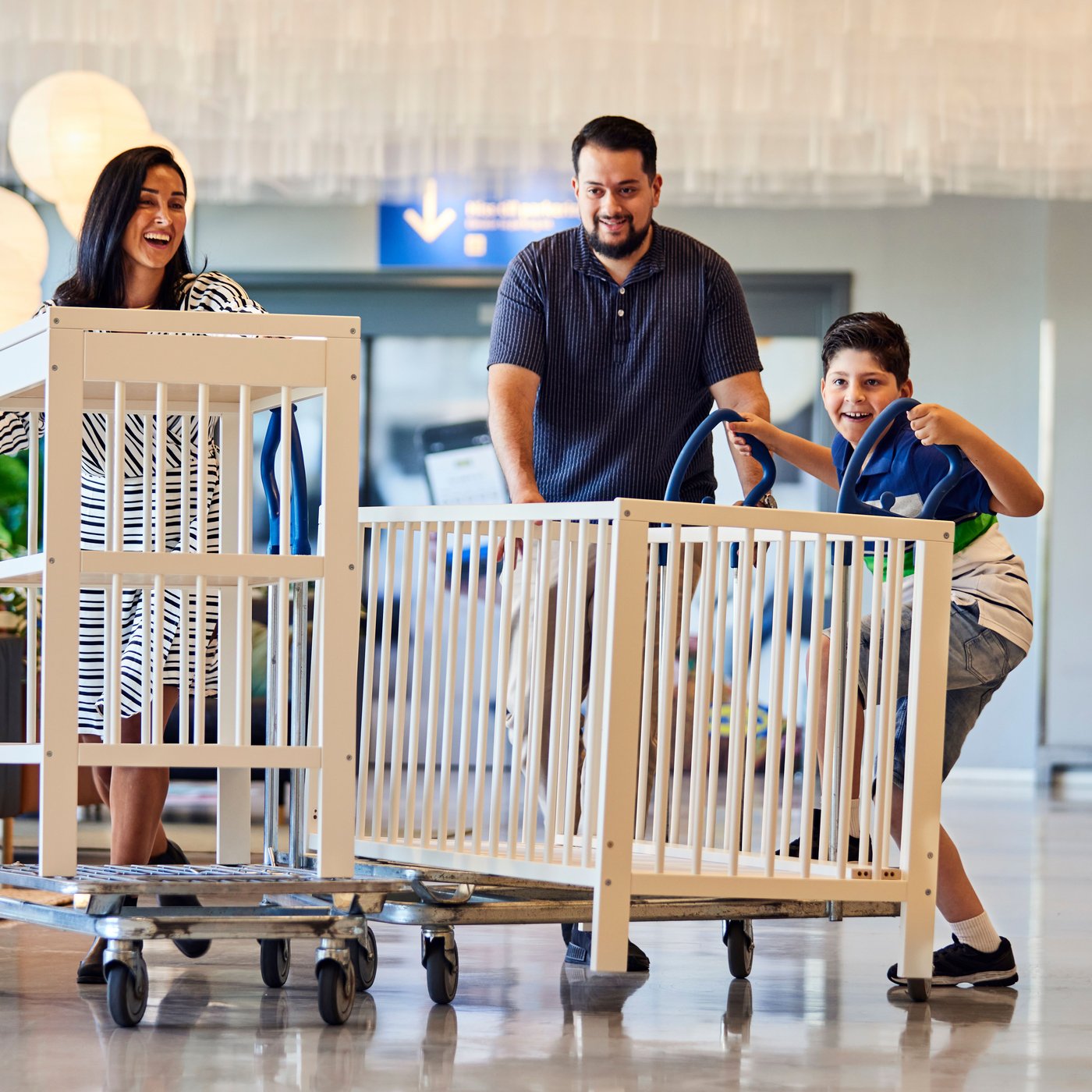 Egy három tagú család használt gyerekágyakat visz lapos bevásárlókocsin egy IKEA áruházban.